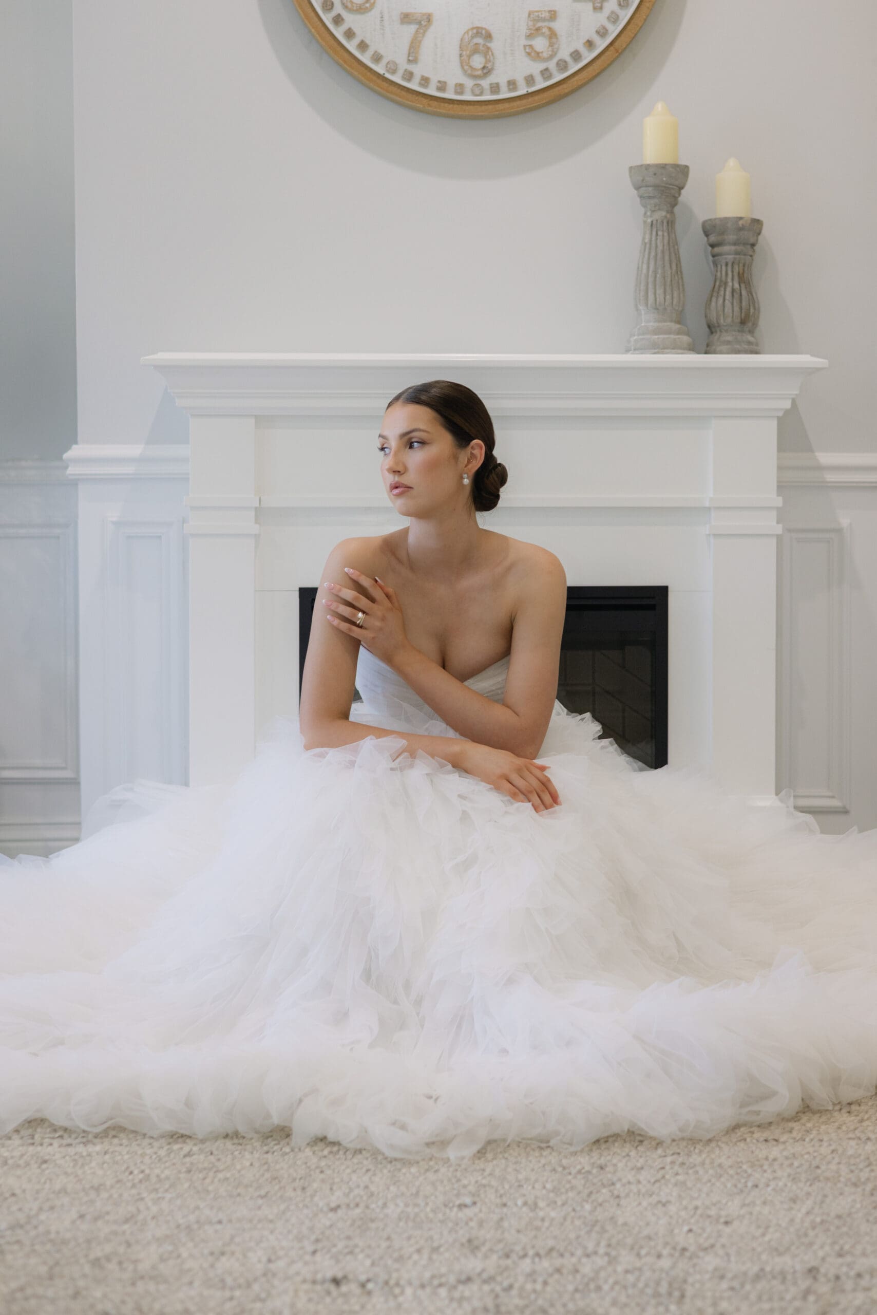 Bride sitting in a tulle wedding gown in front of a white fireplace.